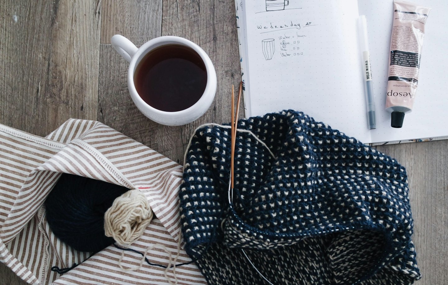 Knitting project with tea and journal on a wooden table.
