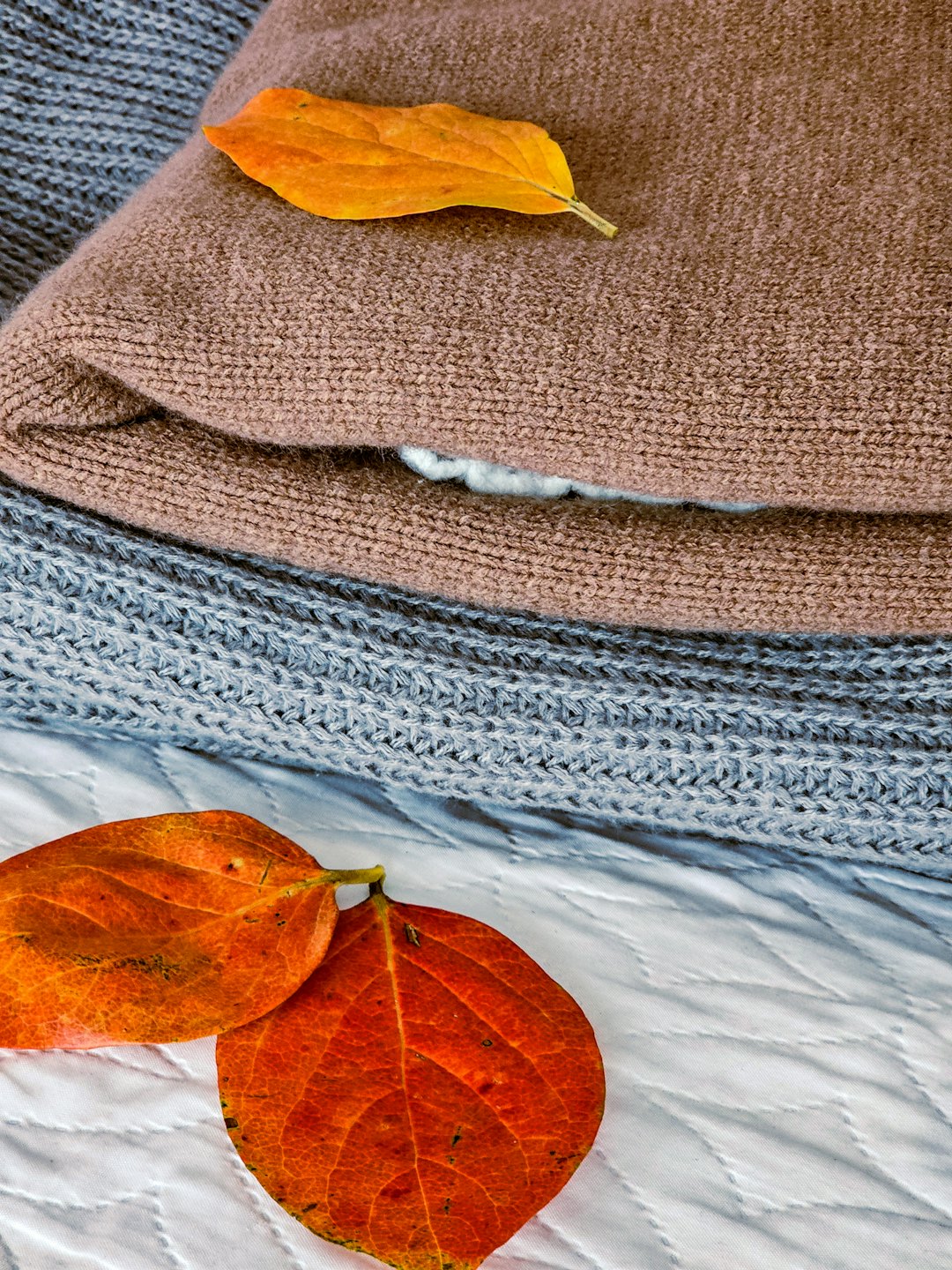 Stack of knitted garments with autumn leaves.