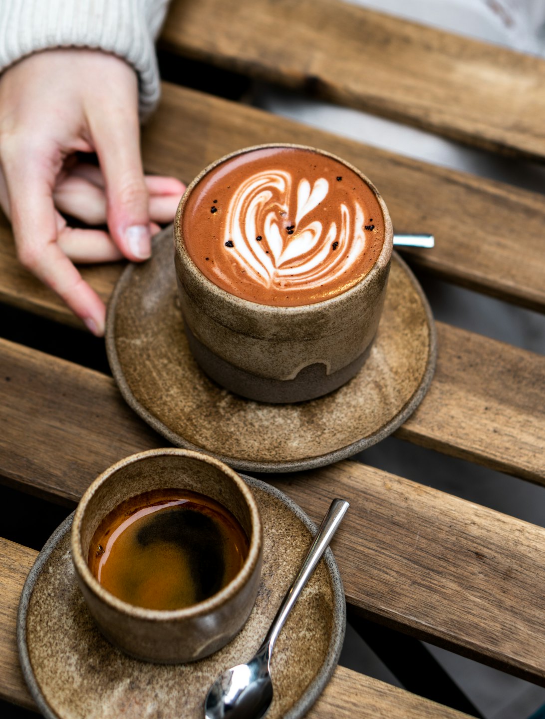 Hand in sweater reaches for coffee on wooden table.